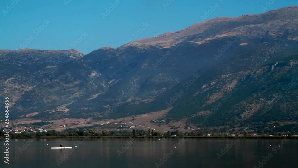 A person is rowing in front of the mountains of the lake of Ioannina in Greece A person is rowing in front of the mountains of the lake of Ioannina in Greece