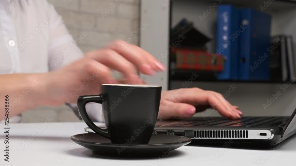 woman drinks hot coffee and works on computer in office. woman drinks hot coffee and works on computer in office.