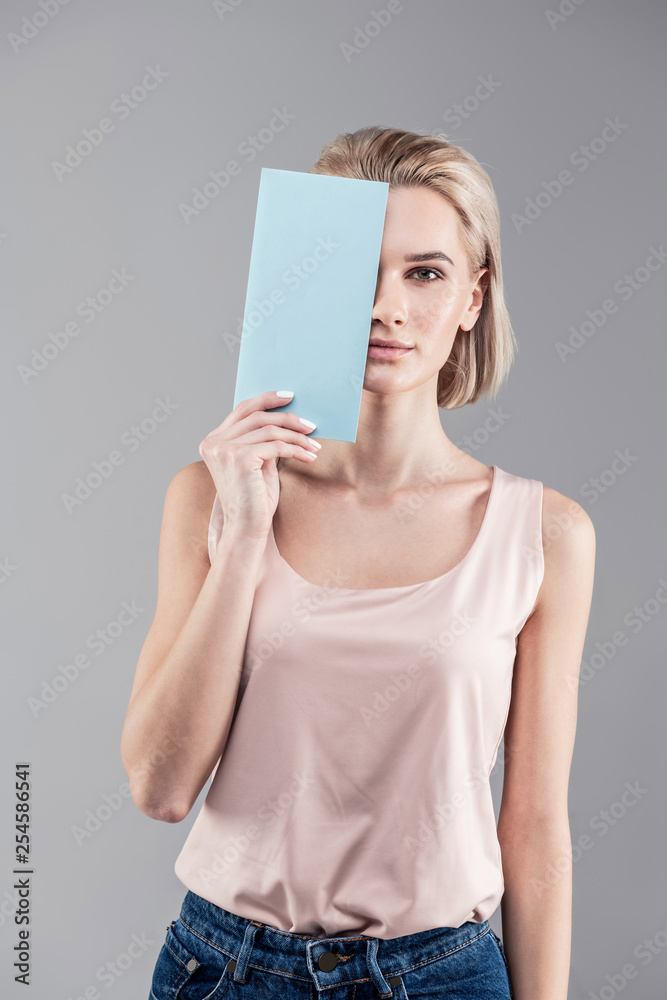 Appealing short-haired woman in jeans and shirt closing half of her face Appealing short-haired woman in jeans and shirt closing half of her face