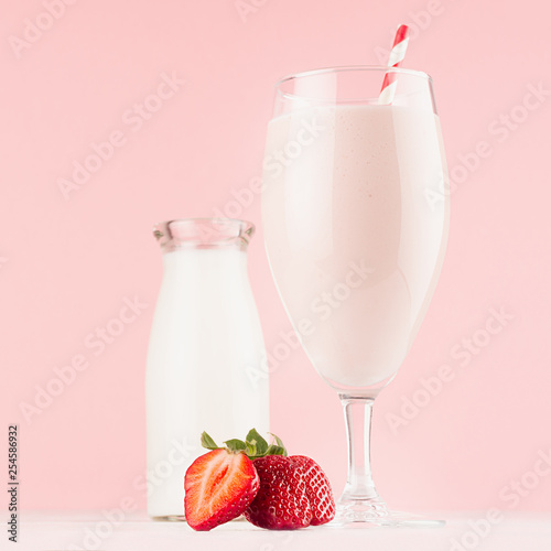 Summer cold fresh dairy cocktail with milk bottle, bright strawberry, straw on white wood board and cute soft pastel pink wall, square.