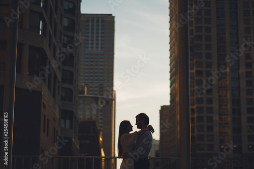 beautiful long-haired girl in summer dress with her handsome husband in white shirt and pants walking in evening Chicago