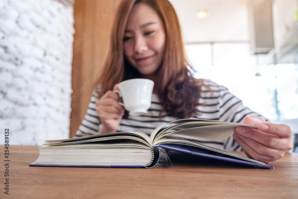 Closeup image of a beautiful asian woman holding and reading a book while drinking coffee Closeup image of a beautiful asian woman holding and reading a book while drinking coffee