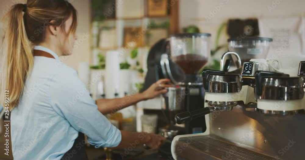 Young attractive female barista grinding coffee beans, barista working in coffee shop, artisan coffee