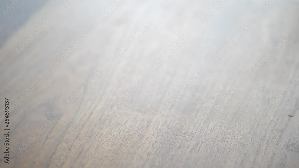 A closeup as a woman's hand picks up a hot steaming cup of tea or coffee from a dining room walnut colored wood table with sunlight coming from a window beyond. A closeup as a woman's hand picks up a hot steaming cup of tea or coffee from a dining room walnut colored wood table with sunlight coming from a window beyond.