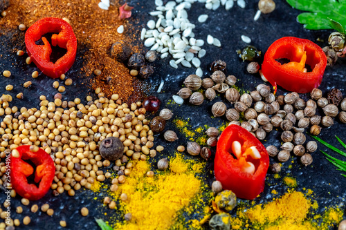 Different kind of spices and herbs and chili on a black stone background