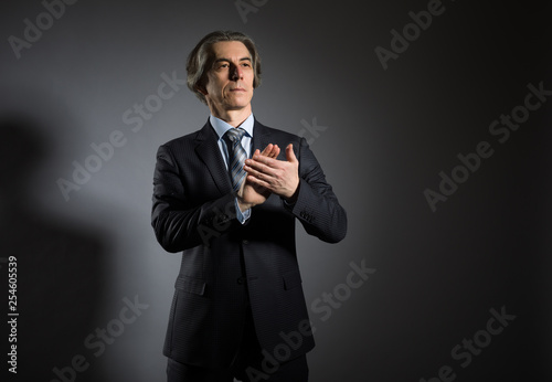 A grown man in an elegant suit claps his hands against a dark background. Businessman applauds.