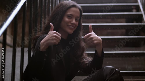 Medium portrait shot of an attractive woman doing a thumbs up gesture to camera. 