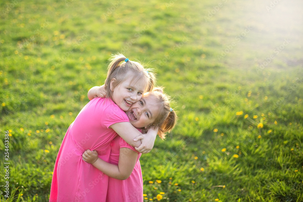 Outdoor portrait of two cheerful pretty girls playing in summer green garden in blossom. Childhood, summer, children games concept