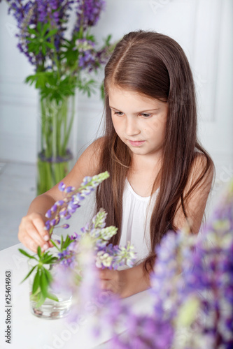 Beautiful littleal girl playing with violet flowers. A flower decor in an interior