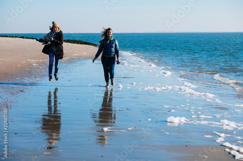 Two friends run along the seashore. Women Friendship. Beach. North Sea. Sunny weather. Coldly.