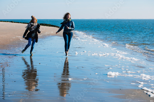 Two friends run along the seashore. Women Friendship. Beach. North Sea. Sunny weather. Coldly.