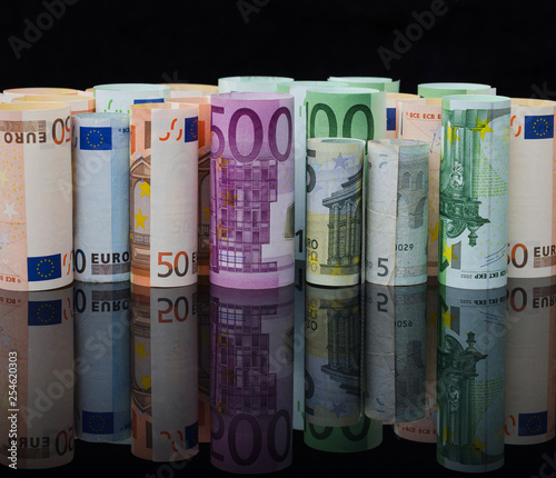 European paper money in rolls on black background with reflection.