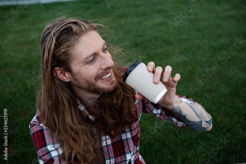 Cheerful long haired man drinking coffee on the grass