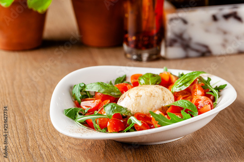 Concept of Italian cuisine. Caprese salad with cherry tomatoes, arugula and basil salad mix, and mozzarella cheese. Serving dishes in white plate in a restaurant. background image.