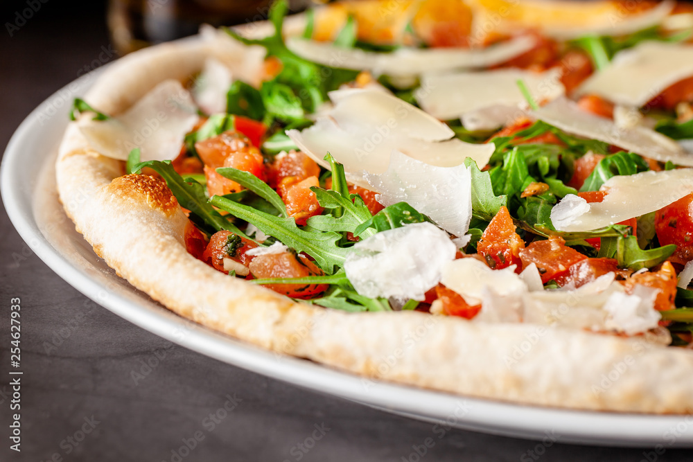 Concept of Italian cuisine. Thin pizza with thick sides with salmon, arugula and cherry tomatoes and parmesan cheese. The chef fills the pizza with garlic oil. Background image. Concept of Italian cuisine. Thin pizza with thick sides with salmon, arugula and cherry tomatoes and parmesan cheese. The chef fills the pizza with garlic oil. Background image.