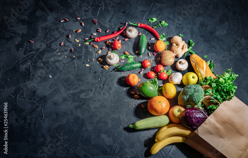 Healthy food in full paper bag of different products vegetables and fruits on dark background