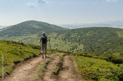 The Young Woman With A Backpack Walking Uphill To Peak Of The Mountain.