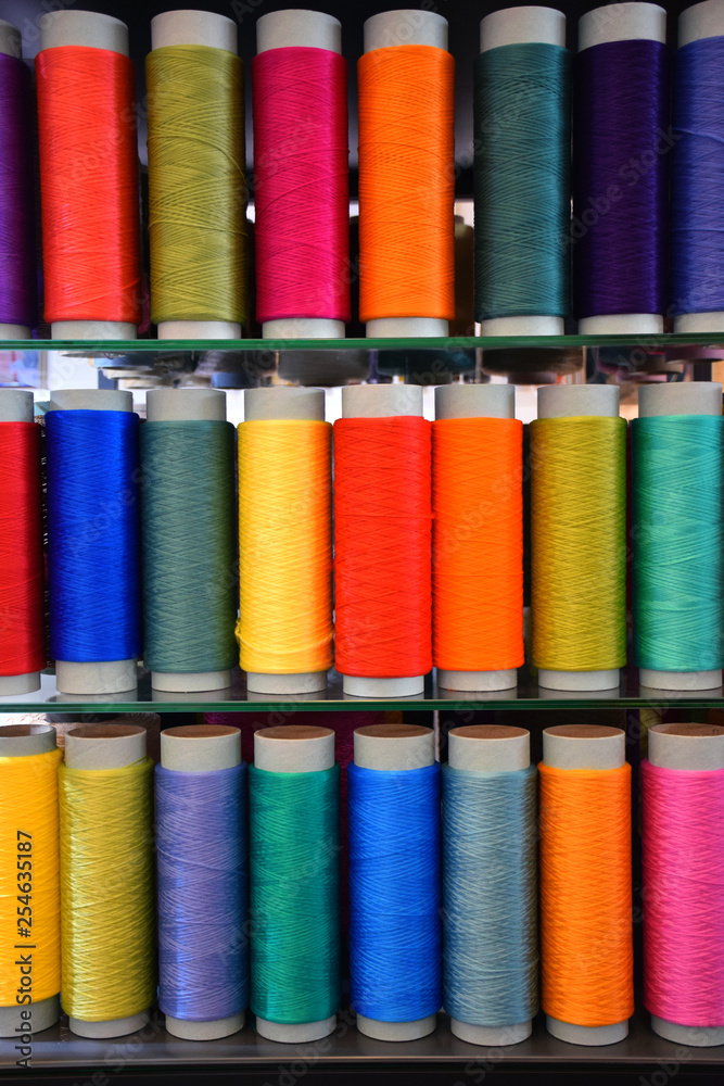 Three rows of vertically placed technical thread bobbins at the exhibition. Polypropylene multifilament yarns. Set of sewing thread coils, miscellaneous colours. Three rows of vertically placed technical thread bobbins at the exhibition. Polypropylene multifilament yarns. Set of sewing thread coils, miscellaneous colours.