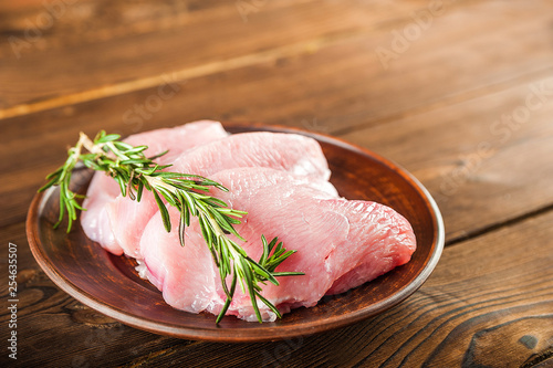 Chicken fillet with rosemary on a wooden plate on a textural table. Raw turkey meat and peppercorns close-up and copy space.