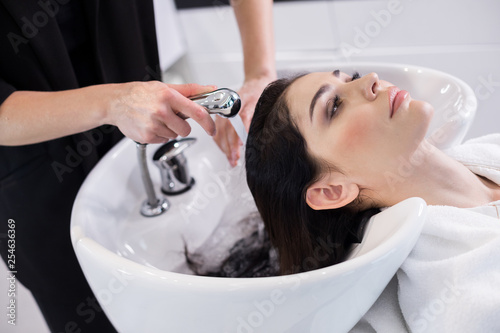Stylist is washing long hair of client in barbershop