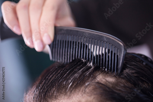 Close up of barber making hairstyle for client using hairbrush in saloon