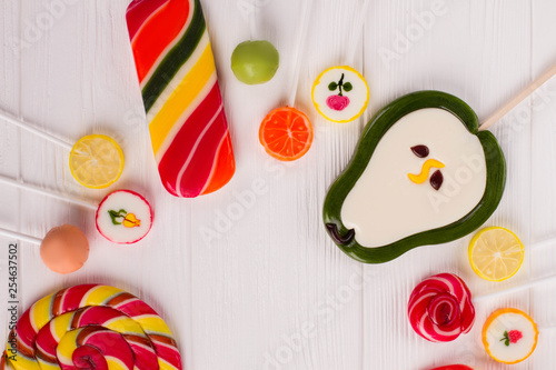Set of various candies on sticks. Frame from colorful lollipops on white wooden background with copy space, top view.
