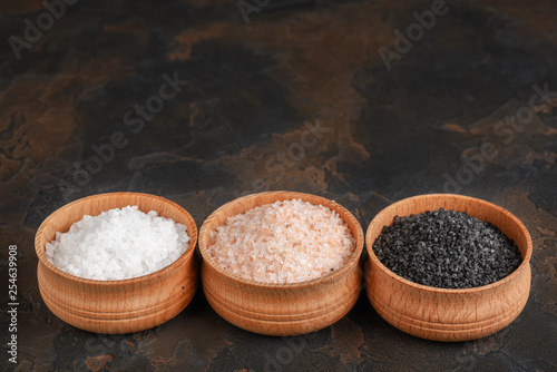 White (sea), pink (himalayan) and black salts in wooden bowls on dark background