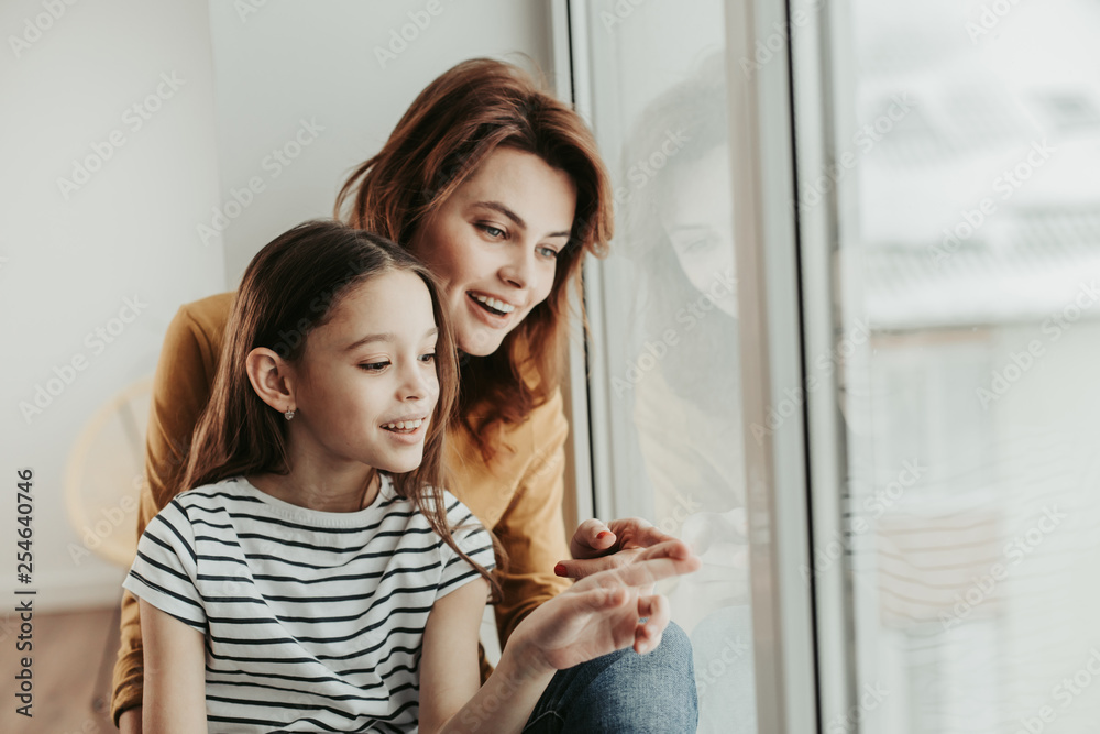 Mother and daughter curiously looking at window Mother and daughter curiously looking at window