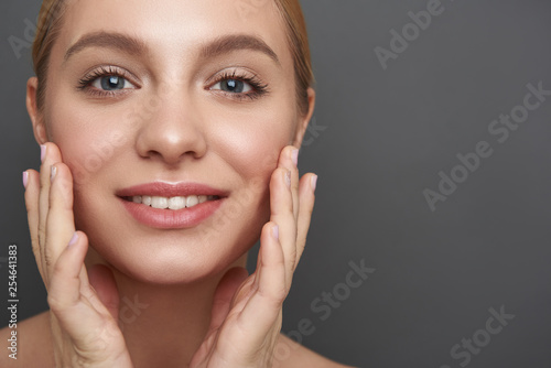 Glad woman touching her skin and smiling cheerfully