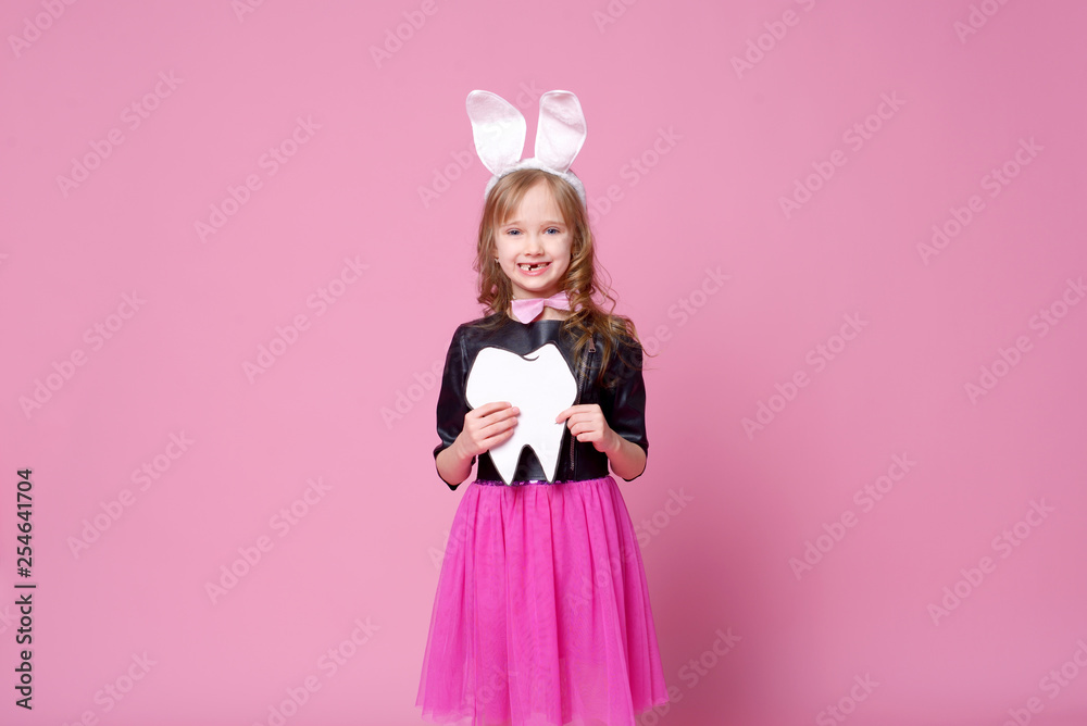 Happy girl in the form of an Easter Bunny with the layout of the human tooth. Milk teeth are changed to permanent. Concept of medicine. Dentist day. Selective focus. Happy girl in the form of an Easter Bunny with the layout of the human tooth. Milk teeth are changed to permanent. Concept of medicine. Dentist day. Selective focus.