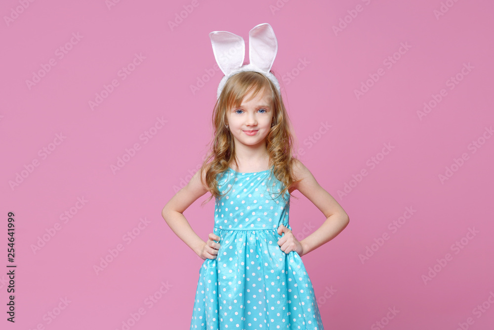 Beautiful blonde in the shape of an Easter Bunny and a blue dress with a pea pattern holds her hands at the waist. Concept of advertising and fashion. Happy Easter. Selective focus.