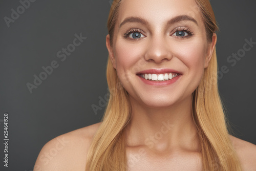 Portrait of positive woman smiling while standing against the grey background