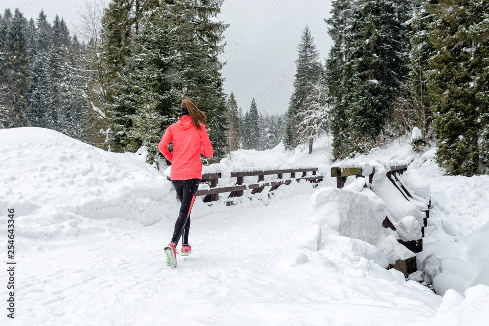 Young woman running on snow in winter mountains wearing warm clothing gloves in snow weather Young woman running on snow in winter mountains wearing warm clothing gloves in snow weather