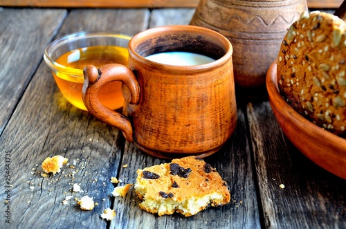 Oatmeal cookies in a ceramic rustic plate, milk in a ceramic mug, napkin, honey on a rustic wooden table. © YUABOG