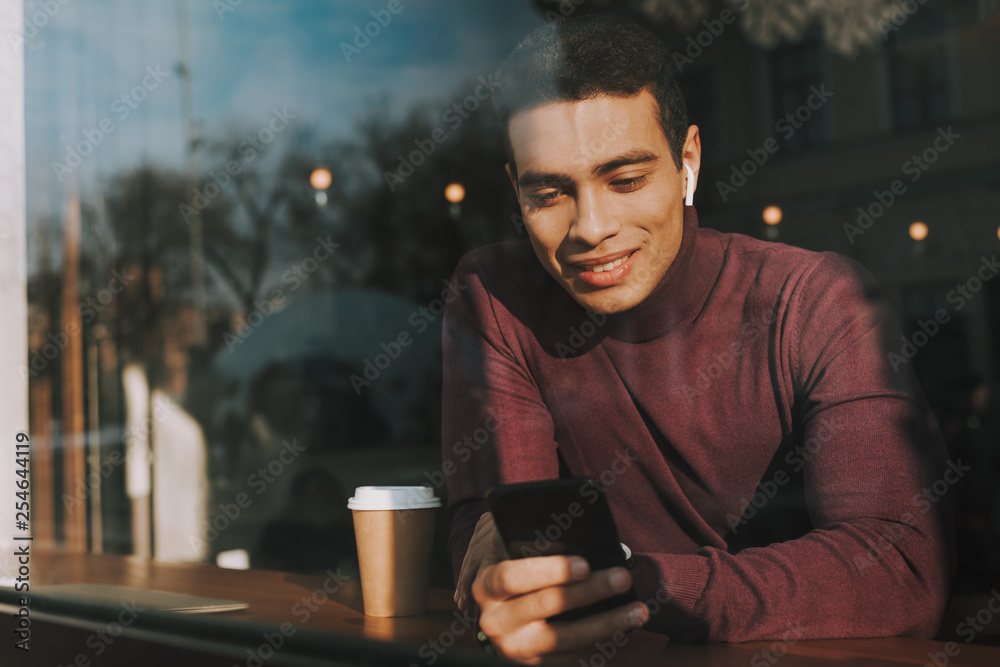 Handsome joyful guy behind glass using cellphone