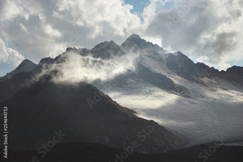 Mountain landscape of a high mountain slope with a cracked glacier muddy volcanic slope against the backdrop of the Caucasus Mountains in the window of clouds. Glaciers of the North Caucasus © yanik88