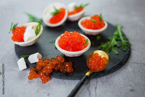 Red caviar on black plate with spoon and creamy cheese. Food photo concept