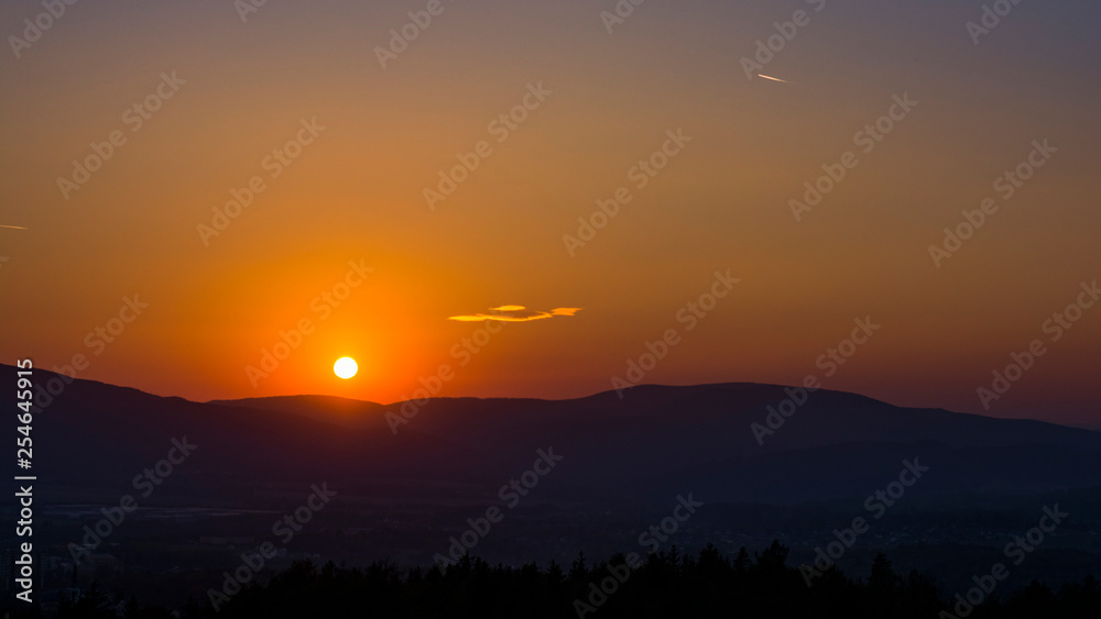 Landscape with the sunset. Clear orange sky with little cloud and dark landscape.
