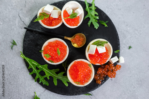 Red caviar on black plate with spoon and creamy cheese. Food photo concept
