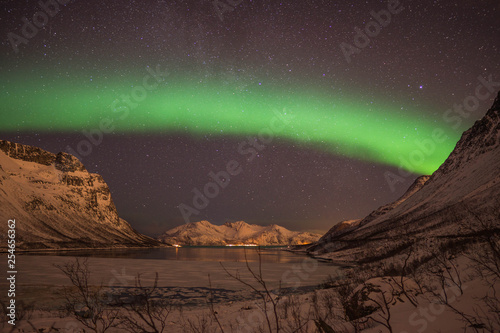 Northern lights - Aurora Borealis in Tromsø, Norway during winter time with a lot of snow on the mountains and big rocks in the foreground and start in the clouds