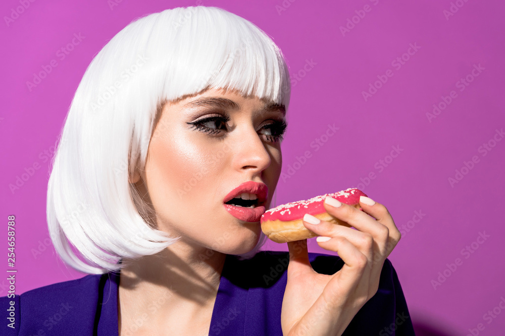 Pretty girl in white wig eating doughnut on purple background Pretty girl in white wig eating doughnut on purple background
