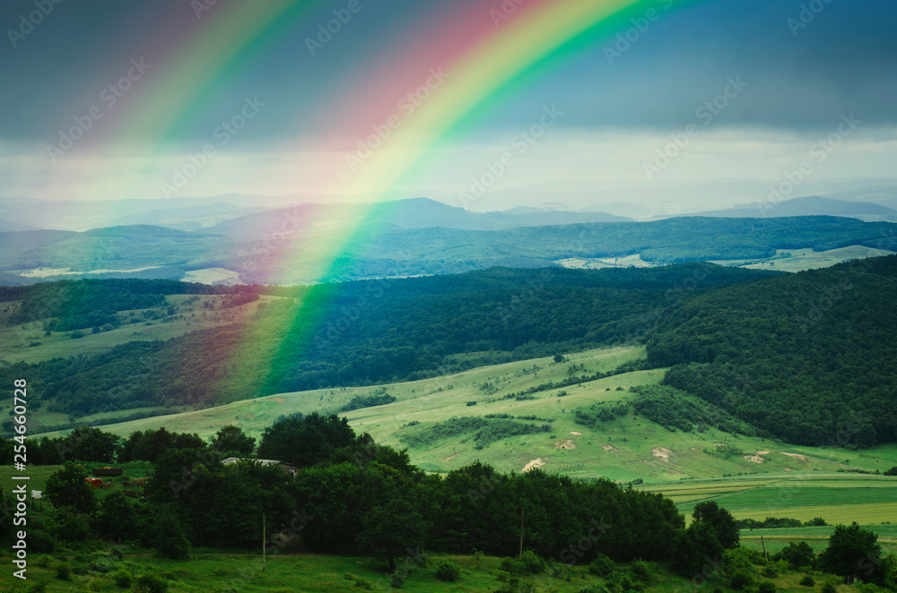 rainbow over beautiful green summer landscape after rain, fresh green meadows and hills in serene landscape