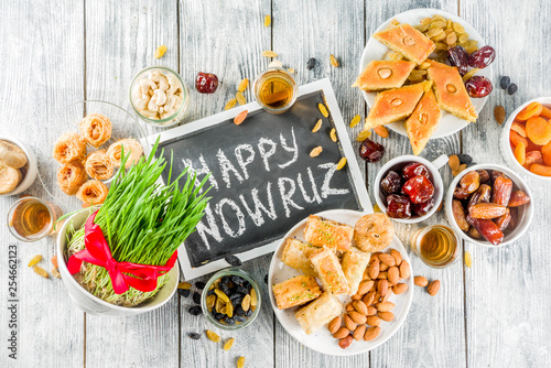 Happy Nowruz holiday background. Celebrating Nowruz sweets and treats- baklava, various dried fruits,  nuts, seeds, wooden background with green grass, copy space
