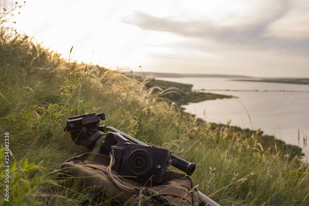 Photo camera on the baclpack and tripod in the mountainst against sunset and river Photo camera on the baclpack and tripod in the mountainst against sunset and river