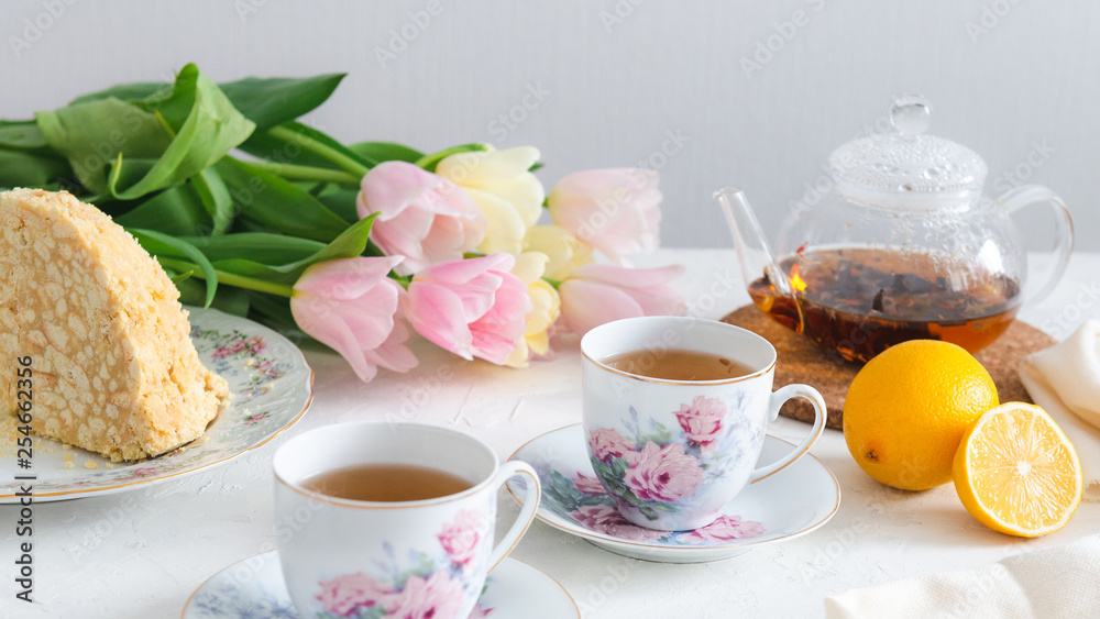 Afternoon tea with cake, lemon, teapot and tulips on the background. Tea party. Spring mood, Mother's day concept Afternoon tea with cake, lemon, teapot and tulips on the background. Tea party. Spring mood, Mother's day concept