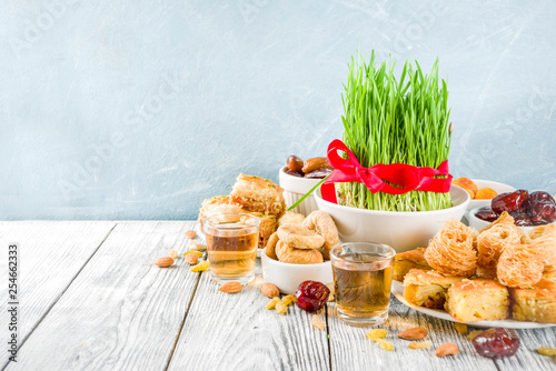 Happy Nowruz holiday background. Celebrating Nowruz sweets and treats- baklava, various dried fruits,  nuts, seeds, wooden background with green grass, copy space photo