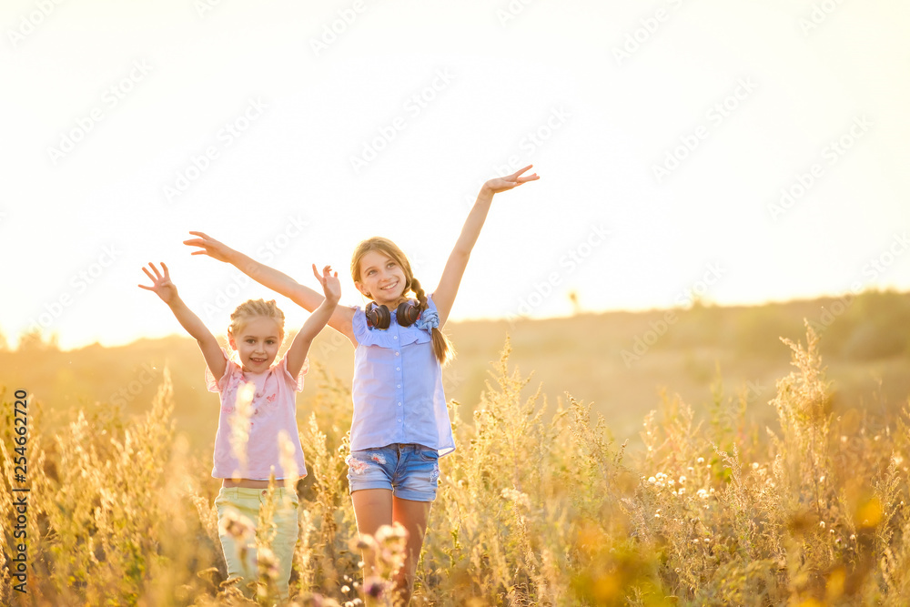Little smiling girls stand on sunshine evening field with joyfully raised hands Little smiling girls stand on sunshine evening field with joyfully raised hands