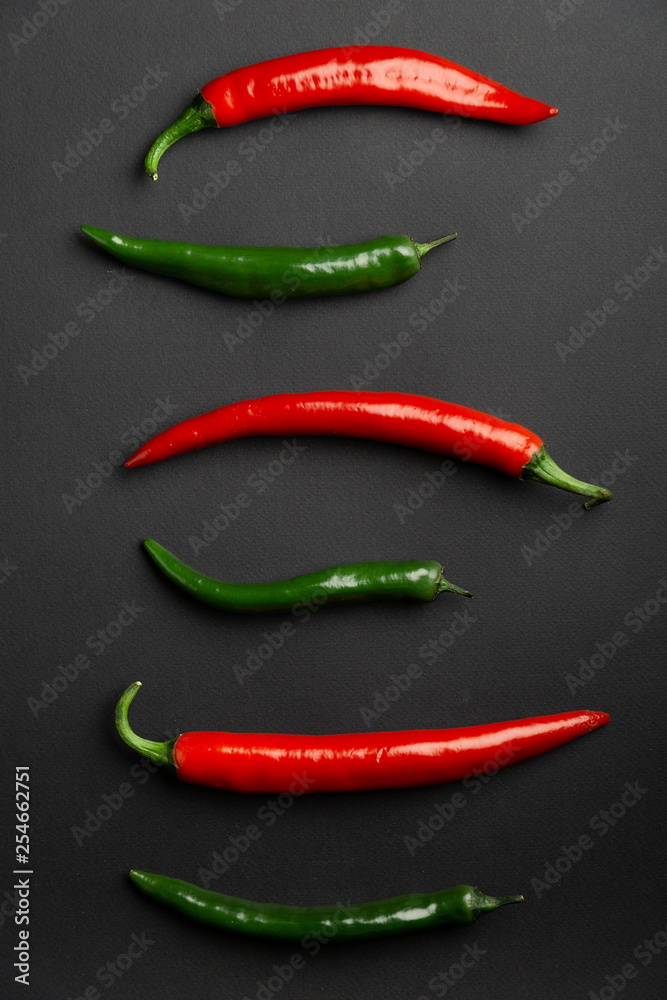 Green and red chili peppers on black background, top view. Hot spicy food symbol.
