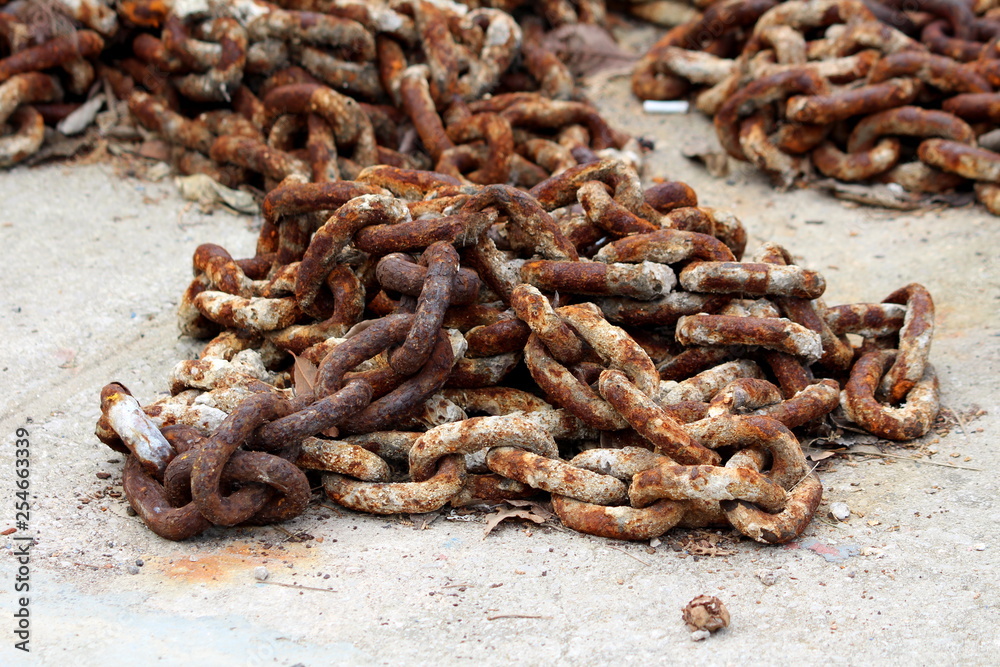 Thick strong rusted metal chain removed from ship anchor and left on concrete pier after being replaced with new and improved version on warm spring day Thick strong rusted metal chain removed from ship anchor and left on concrete pier after being replaced with new and improved version on warm spring day