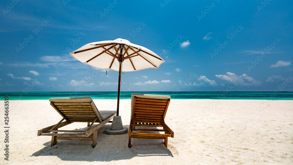 Romantic beach scene, two lounge chairs and umbrella on white sand. Honeymoon or vacation concept, couple and luxury travel background
